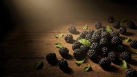 Fresh blackberries with green leaves scattered on rustic wooden surface, ideal for food photography, culinary blogs, recipe websites, and organic produce marketing materials.
