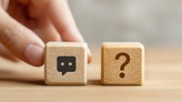Hand holding wooden cube with chat icon next to question mark cube on wooden surface, representing communication and customer support concepts.