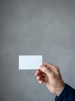 Male hand holding blank white business card against neutral gray background, suitable for branding, corporate identity, and marketing mockup designs.
