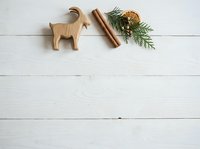 Wooden goat figurine, cinnamon stick, and evergreen sprigs with dried citrus on white wooden surface for holiday styling and seasonal design projects.