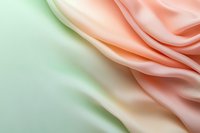 Soft flowing fabric in peach and mint green creates gentle waves and folds, abstract background with smooth silky texture and pastel gradient colors.