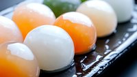 Fresh white and orange spherical mochi desserts arranged on dark plate with water droplets, showcasing traditional Japanese sweets in modern presentation.