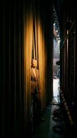 Professional actress standing backstage between golden curtains with stage lighting equipment and dramatic shadows creating theatrical atmosphere.