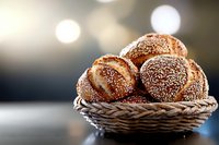 Fresh baked bread rolls with sesame and poppy seeds in rustic woven basket against blurred bokeh background, warm morning light creates cozy atmosphere.