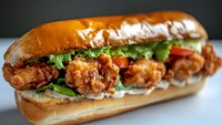Crispy fried shrimp po boy sandwich with fresh lettuce, tomatoes and creamy sauce on toasted baguette roll, close up view of classic Louisiana cuisine.