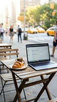 Laptop and croissant on wooden outdoor table with coffee cup in urban street setting, blurred city background with yellow taxis and pedestrians, remote work and freelance lifestyle concept.