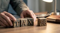 Accountant arranging wooden blocks spelling tax and percentage symbol on desk, representing financial planning and tax calculation services for business.
