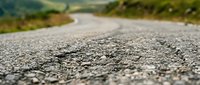 Close-up view of asphalt road surface with gravel texture and blurred landscape background. Use for transportation, infrastructure, travel, and construction projects.