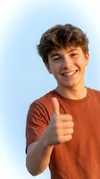 Happy teenage boy giving thumbs up gesture with bright smile against clear blue sky background for positive youth and success concepts.