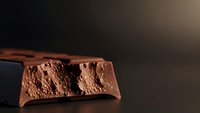 Broken chocolate bar with aerated bubbles texture on dark background. Sweet confectionery dessert with porous structure for food photography and culinary design.