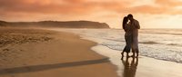 Romantic couple silhouette embracing on beach at golden sunset with ocean waves and dramatic sky creating intimate moment for love and relationship concepts.