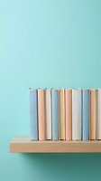 Row of colorful books arranged on wooden shelf against mint green wall background for education and reading concepts.
