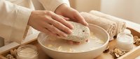 Woman hands kneading dough in ceramic bowl on wooden table with flour, milk and walnuts for homemade bread baking in warm kitchen atmosphere.