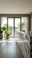 Modern kitchen island with marble countertop and tropical plants near large windows overlooking outdoor terrace in contemporary home interior design.