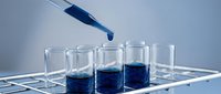 Laboratory pipette dispensing blue liquid into glass test tubes in scientific research setting for medical analysis and chemical experiments.