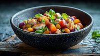 Fresh shrimp ceviche with colorful bell peppers, cherry tomatoes and basil served in black textured bowl on rustic wooden table with water drops.