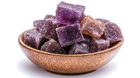 Purple and brown sugar candy cubes dusted with powdered sugar in rustic ceramic bowl on white background, sweet dessert confectionery closeup.