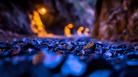 Dramatic close-up of wet cobblestone street at night with glowing orange streetlights creating bokeh effect against dark blue stones, moody urban atmosphere.