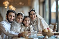 Happy Middle Eastern family enjoying meal together at home, parents with two daughters in traditional dress sharing authentic cultural moment during dinner gathering.