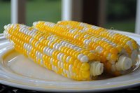 Fresh corn on the cob with butter melting on white plate, ready for summer dining and meal preparation.