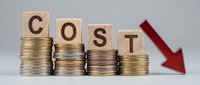 Business cost reduction concept with wooden letter blocks spelling COST on decreasing coin stacks and red downward arrow on white background.