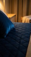 Blue pillow on quilted bedding in warm-lit bedroom with golden curtains. Cozy hotel or home interior design, relaxation and comfort concept for hospitality and lifestyle use.