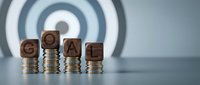 Wooden blocks spelling GOAL on stacked coins with target background representing financial planning and achievement strategy for business success.