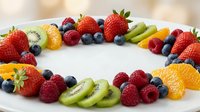 Colorful fresh fruit platter arranged in circle with strawberries, blueberries, raspberries, kiwi and orange slices on white plate for healthy eating and party catering.