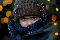 Young woman with blue eyes wearing knit hat and scarf in winter snow with warm bokeh lights creating cozy holiday atmosphere for seasonal campaigns.