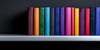 Colorful hardcover books arranged in rainbow order standing on white shelf against dark background, creating minimalist library display for education concepts.