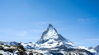 Iconic snow-capped mountain peak with distinctive pyramidal shape against clear blue sky, surrounded by alpine landscape and glaciers. Suitable for travel, nature, and outdoor adventure projects.