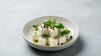 Fresh white cheese cubes with herbs and olive oil served in ceramic bowl on gray background for Mediterranean cuisine and healthy eating.