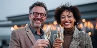 Happy mature couple celebrating with champagne glasses on rooftop terrace during golden hour. Professional business attire, joyful expressions, urban setting.