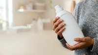 Person of African descent holding white cleaning product bottle in modern kitchen environment for household cleaning and domestic care purposes.