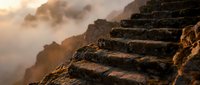 Ancient stone steps carved into rocky cliff face during golden hour sunrise with dramatic misty mountain landscape in background creating mystical atmospheric mood.