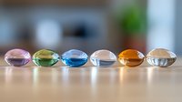 Colorful glass beads in pastel and amber tones arranged in line on wooden surface with soft blur background, creating minimalist composition for design projects.
