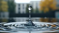 Water drop collision creating crown splash formation with concentric ripples on liquid surface against blurred autumn background. Macro photography captures frozen motion.