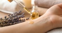 Woman applying lavender essential oil from glass dropper bottle onto hand for aromatherapy skincare treatment and natural wellness routine.