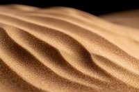 Golden sand dunes create smooth flowing curves and ripples in desert landscape, with fine grains catching soft light against dark background, showing natural patterns.