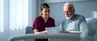 Young female healthcare worker in burgundy scrubs consulting with elderly Caucasian male patient on light blue couch in bright medical office setting.