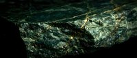 Close-up of raw mineral ore with metallic luster and crystalline structure, featuring green and gold tones. Suitable for geology, mining, and educational materials.