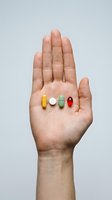 Open hand holding four colorful pills and one white tablet on palm against neutral background, representing medication, healthcare, pharmaceuticals, and wellness treatment options.