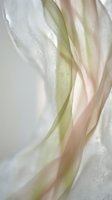 Soft flowing silk fabric in pastel green and pink tones with delicate translucent texture creating elegant waves and folds for luxury fashion design.