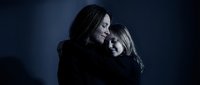 Mother and daughter embracing in tender moment against dark blue background. Emotional family bond, love and care between generations in intimate portrait.