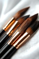 Close-up of professional art brushes with copper ferrules and black handles on white fabric, suitable for fine art, watercolor, and acrylic painting.