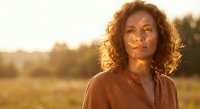 African American woman with curly hair in warm golden sunset light outdoors. Natural portrait photography for lifestyle and wellness content.