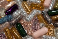 Colorful glitter capsules and pills scattered together, sparkling with metallic and sequin textures in pink, gold, green, and purple tones.