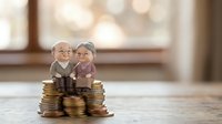 Elderly couple figurines sitting on stacks of coins representing retirement savings, pension planning and financial security for senior citizens.