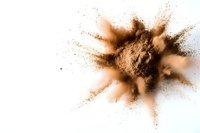 Brown powder explosion on white background, dynamic motion freeze photography capturing dust particles bursting outward in abstract pattern.