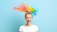 Young Caucasian woman with colorful powder paint explosion in hair laughing joyfully against blue background. Creative hair color concept showing happiness and fun.